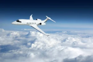A white private jet flying above clouds against a deep blue sky, illustrating the luxury and speed associated with empty leg charters.